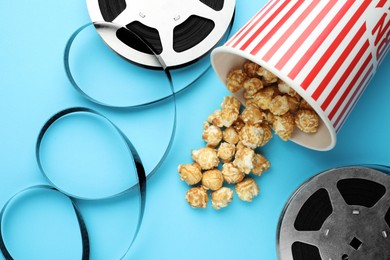 Photo of Sweet popcorn and film reels on light blue background, flat lay