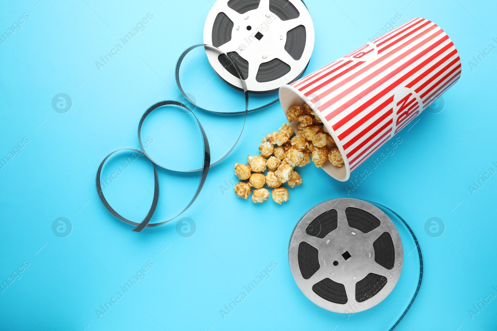 Photo of Sweet popcorn and film reels on light blue background, flat lay