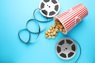 Photo of Sweet popcorn and film reels on light blue background, flat lay