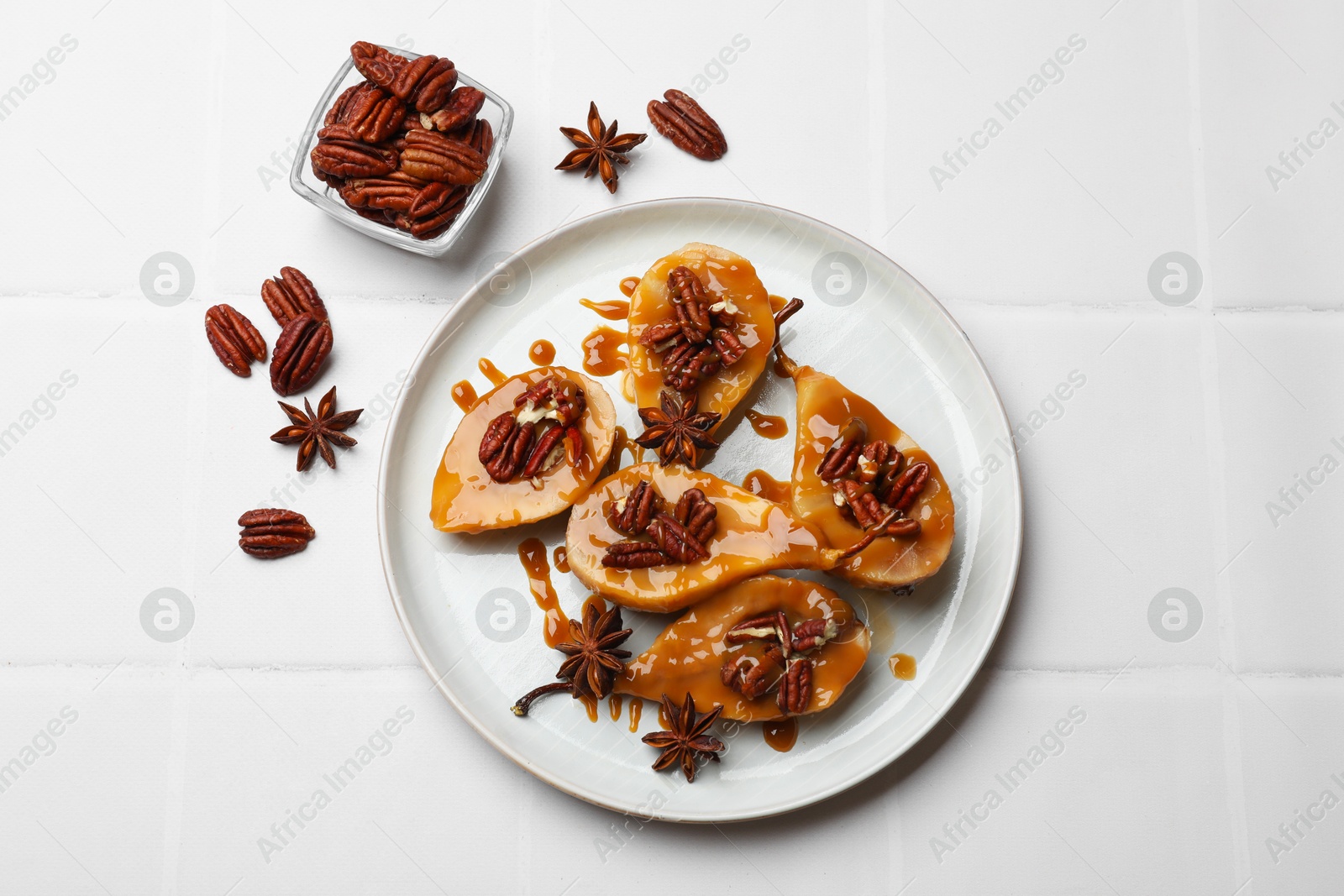 Photo of Delicious pears with caramel sauce, pecan nuts and anise stars on white tiled table, top view