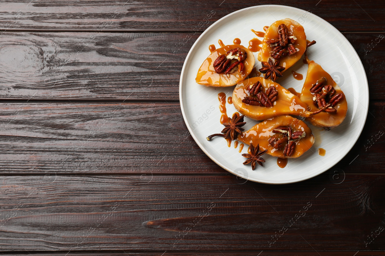 Photo of Delicious pears with caramel sauce, pecan nuts and anise stars on wooden table, top view. Space for text