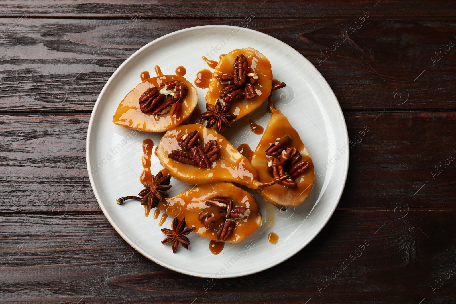 Photo of Delicious pears with caramel sauce, pecan nuts and anise stars on wooden table, top view