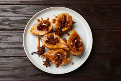 Photo of Delicious pears with caramel sauce, pecan nuts and anise stars on wooden table, top view