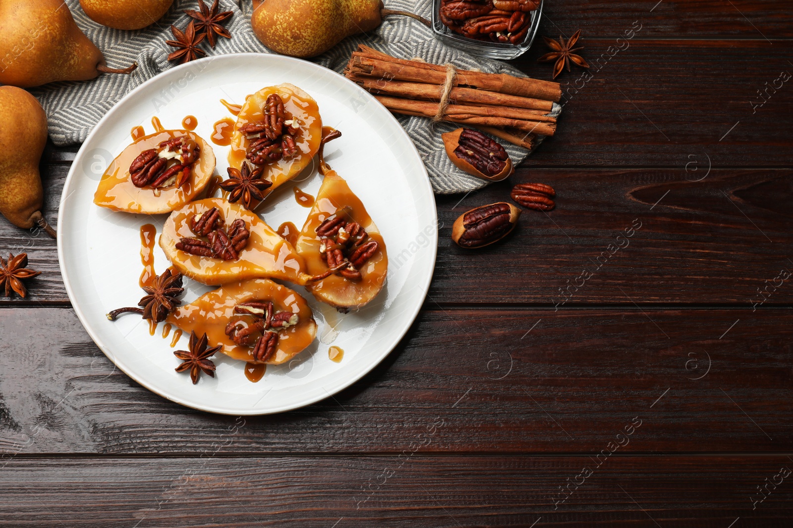 Photo of Delicious pears with caramel sauce, pecan nuts and spices on wooden table, top view. Space for text