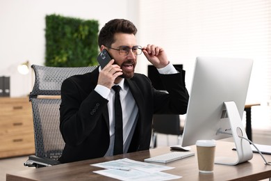 Photo of Man talking on smartphone while working at table in office