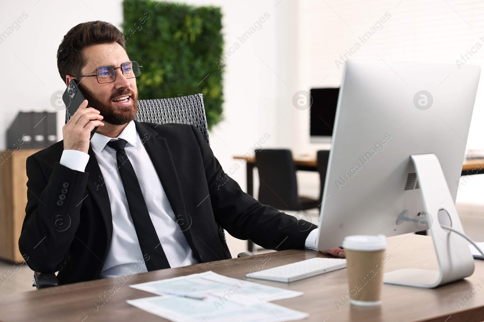 Photo of Man talking on smartphone while working at table in office