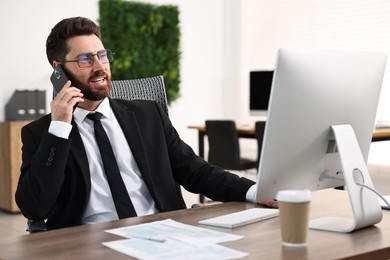 Photo of Man talking on smartphone while working at table in office