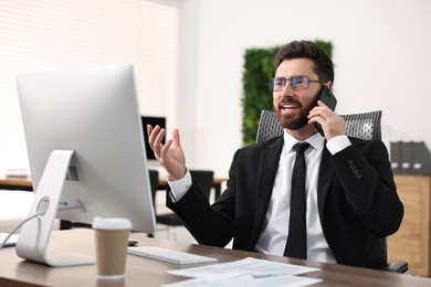 Photo of Man talking on smartphone while working at table in office