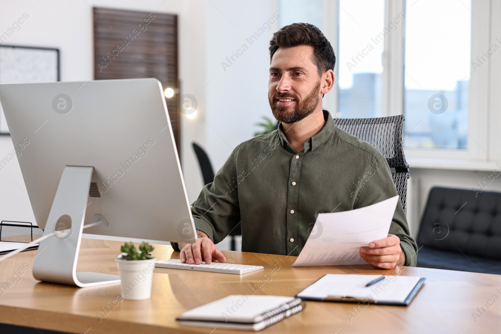 Photo of Man with document working on computer at table in office