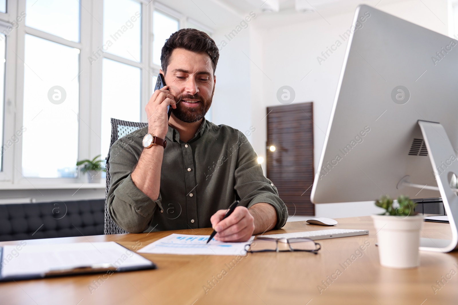 Photo of Man talking on smartphone while working at table in office