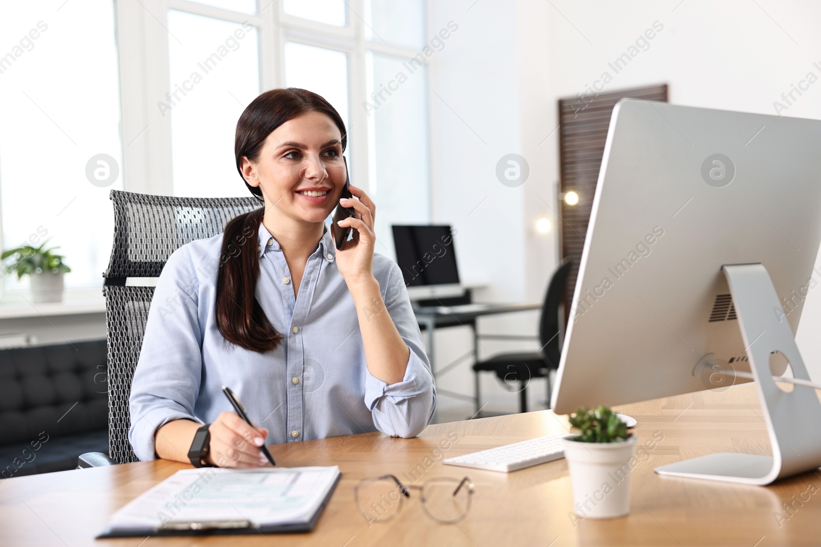 Photo of Woman talking on smartphone while working at table in office