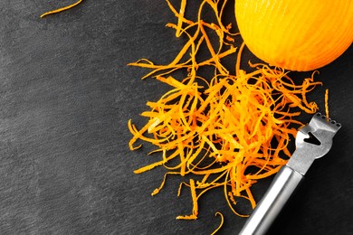 Photo of Fresh orange zest, zester and fruit on black table, flat lay. Space for text