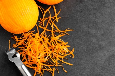 Photo of Fresh orange zest, zester and fruit on black table, flat lay. Space for text