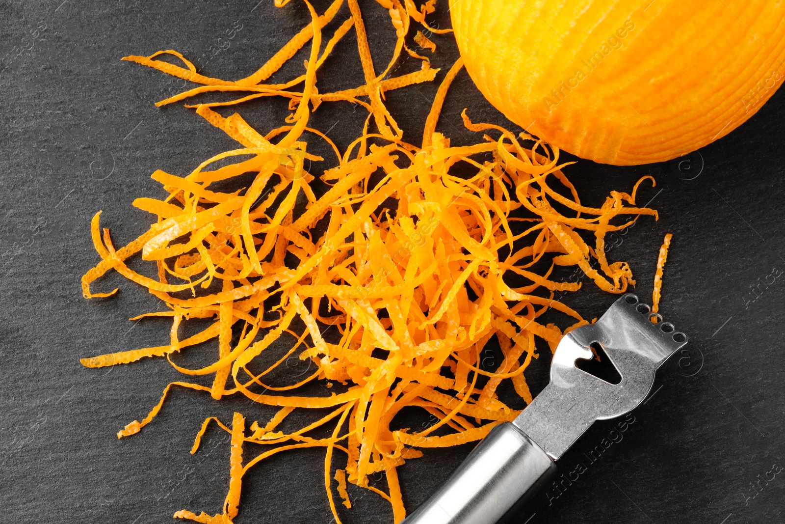 Photo of Fresh orange zest, zester and fruit on black table, flat lay