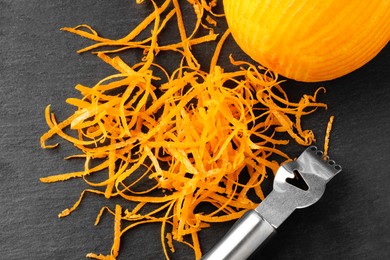 Photo of Fresh orange zest, zester and fruit on black table, flat lay