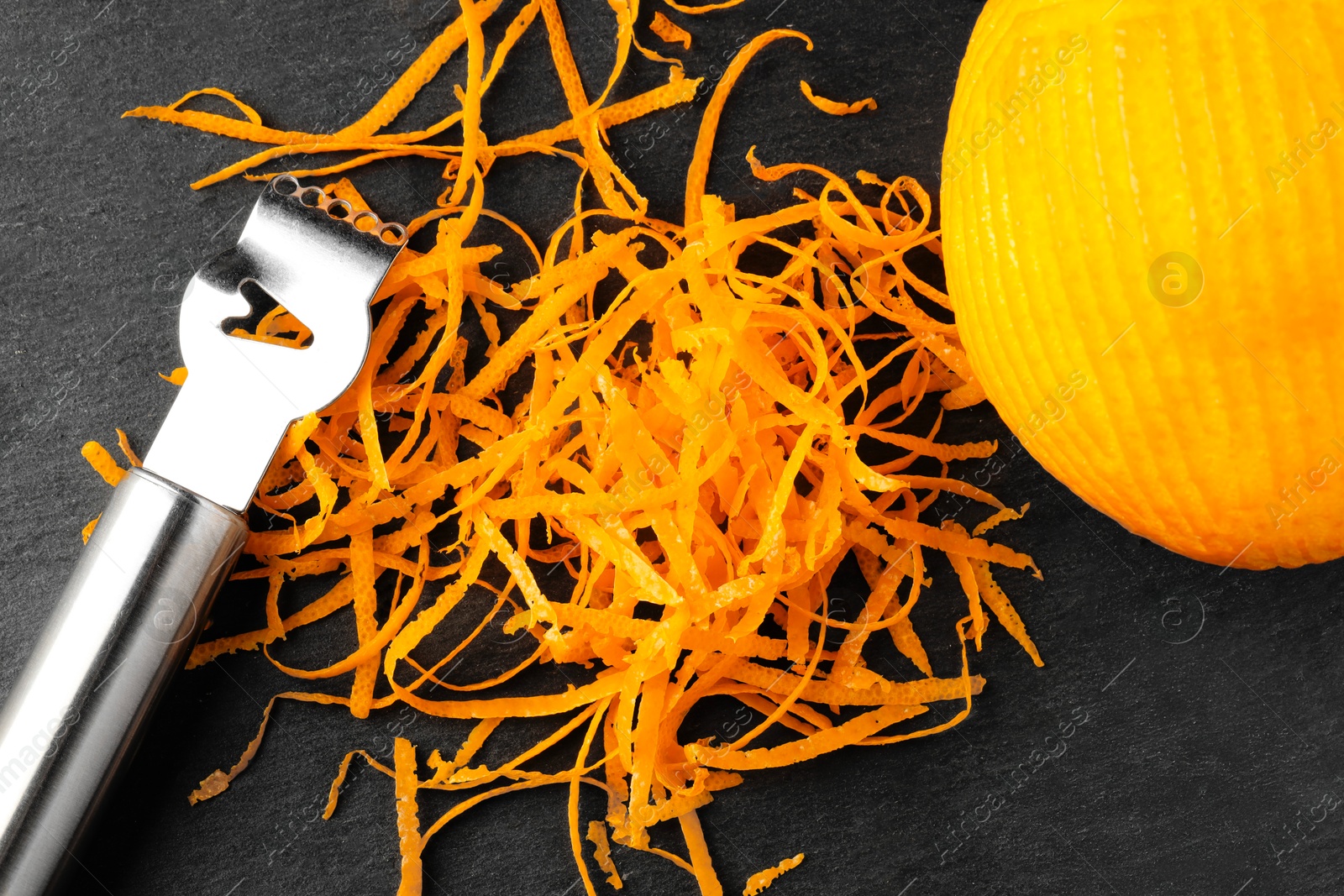 Photo of Fresh orange zest, zester and fruit on black table, flat lay