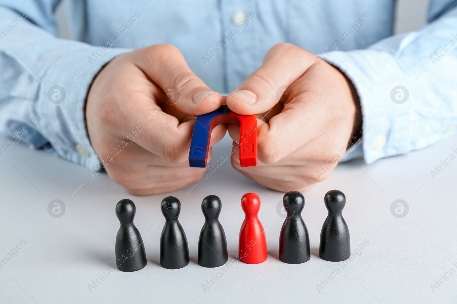 Photo of Man with magnet attracting game pieces at white table, closeup