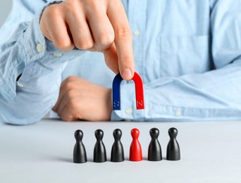 Photo of Man with magnet attracting game pieces at white table, closeup