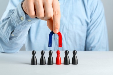 Photo of Man with magnet attracting game pieces at white table, closeup