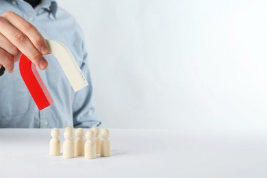 Photo of Man with magnet attracting game pieces at white table, closeup. Space for text