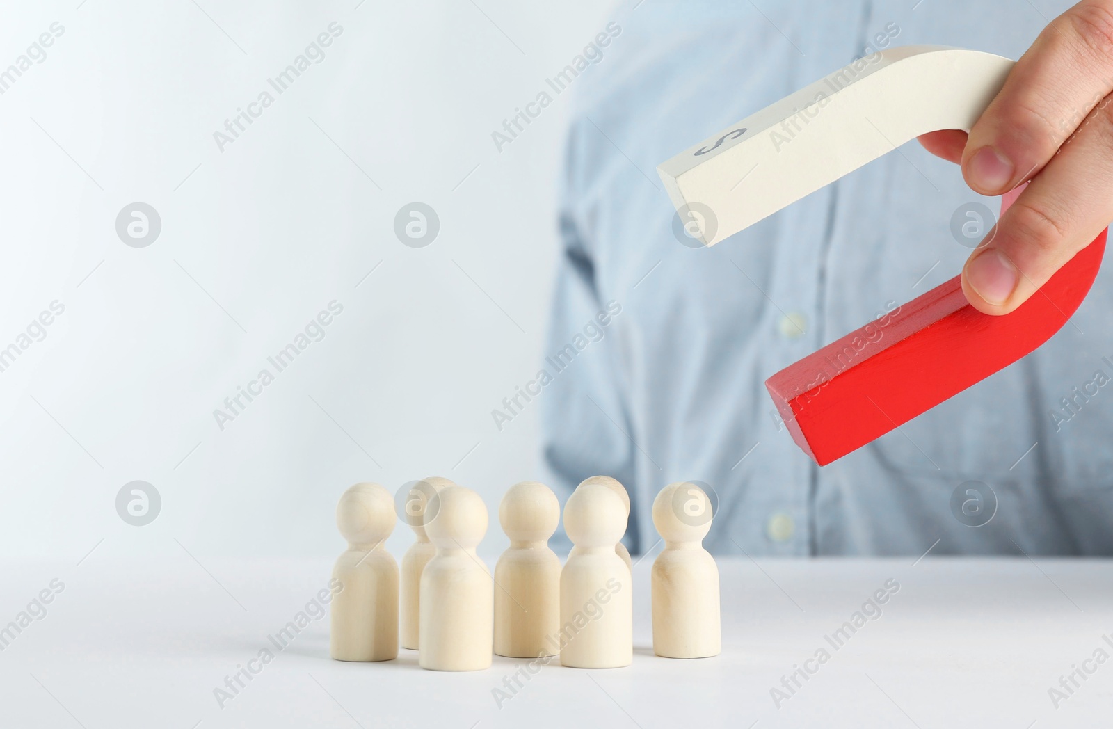 Photo of Man with magnet attracting game pieces at white table, closeup. Space for text