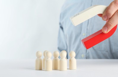 Photo of Man with magnet attracting game pieces at white table, closeup. Space for text