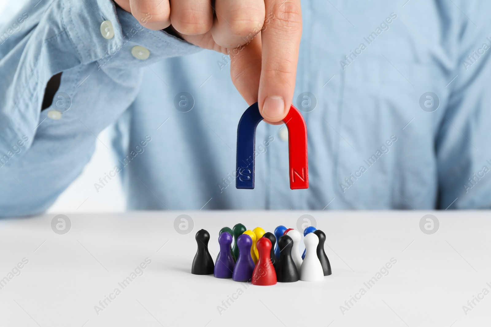 Photo of Man with magnet attracting game pieces at white table, closeup