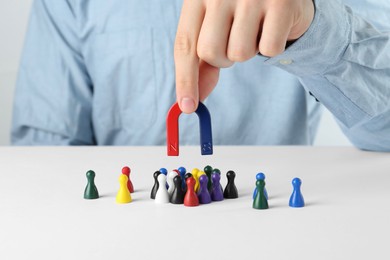 Photo of Man with magnet attracting game pieces at white table, closeup