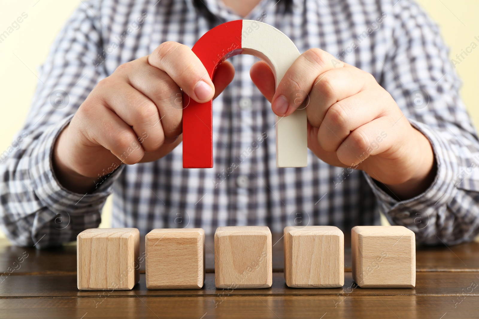 Photo of Man with magnet attracting cubes at wooden table, closeup