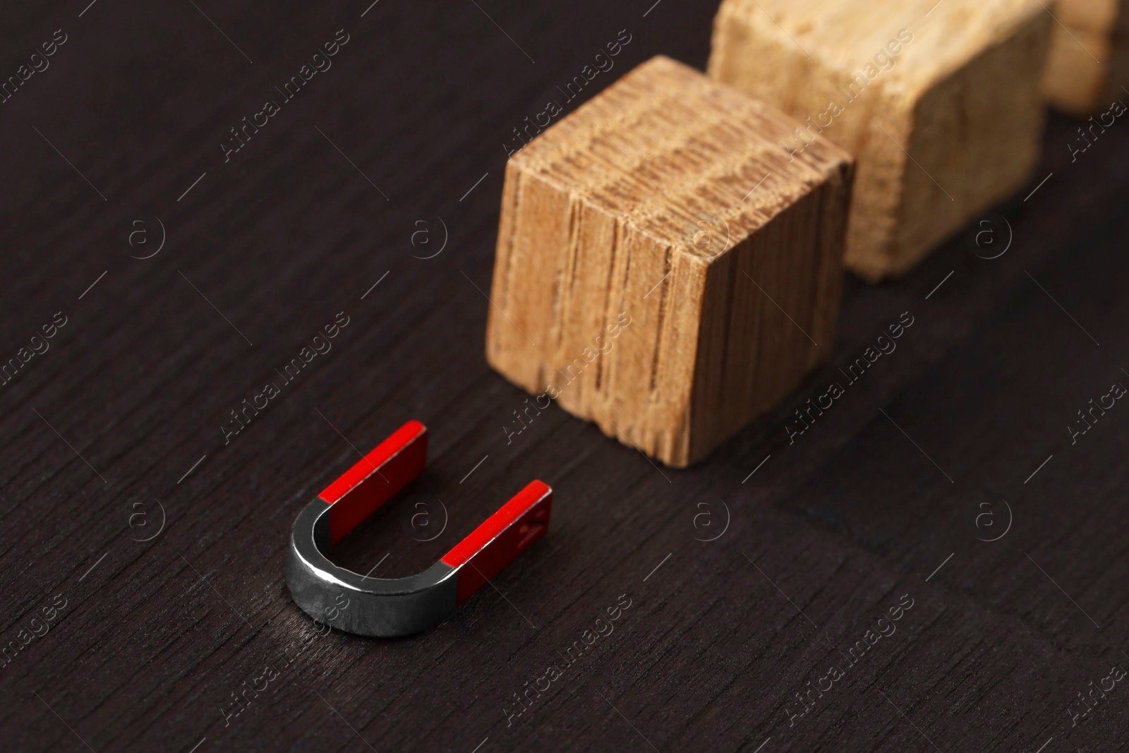 Photo of Magnet attracting cubes on black wooden table, closeup