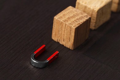 Photo of Magnet attracting cubes on black wooden table, closeup