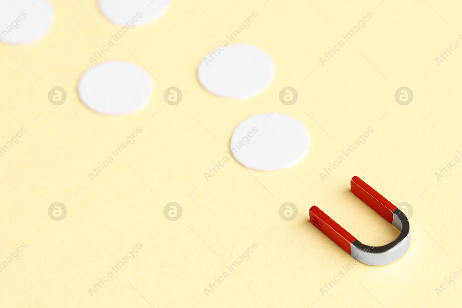 Photo of Magnet attracting paper circles on beige background, closeup