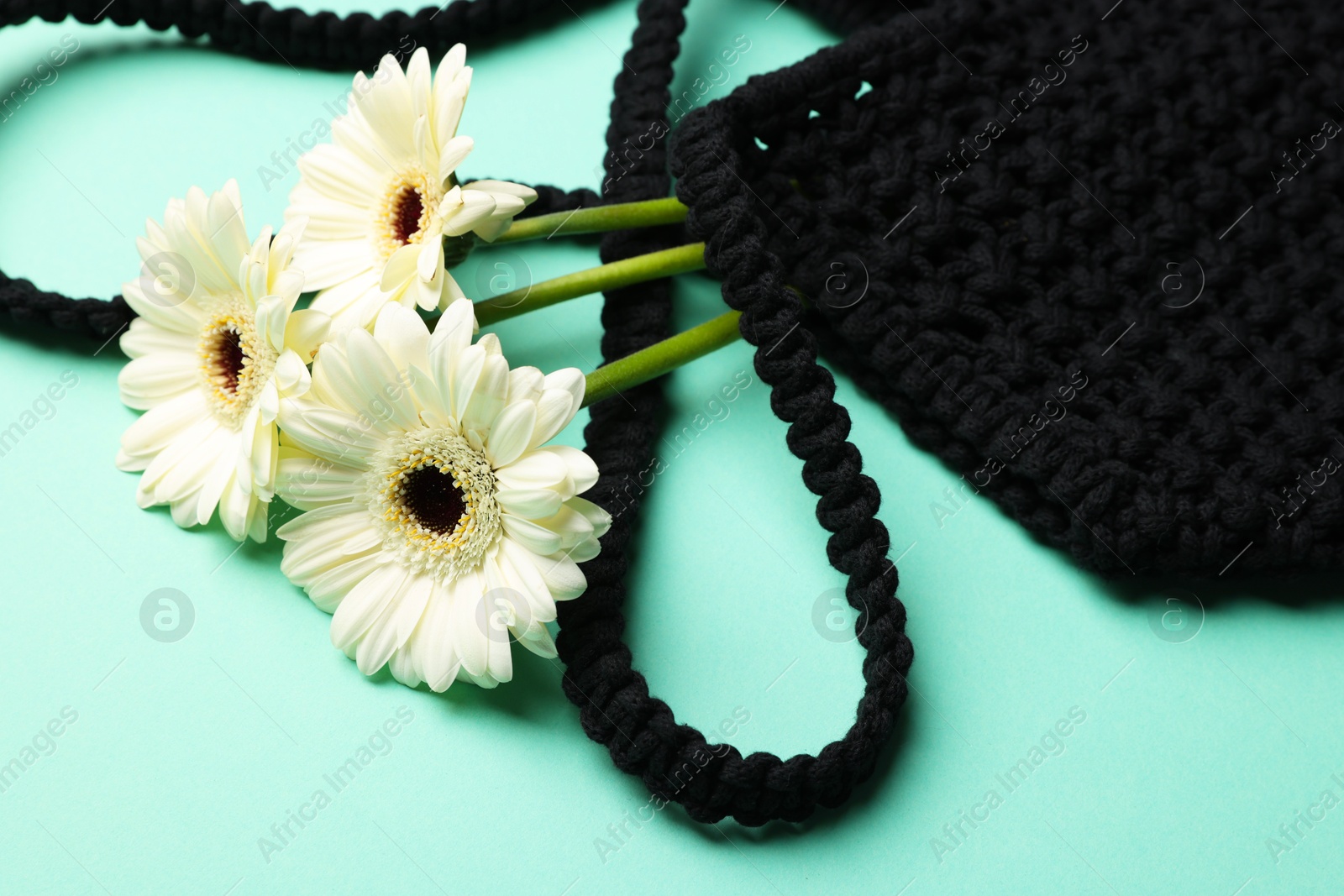 Photo of Macrame shopping bag with beautiful flowers on turquoise background, closeup