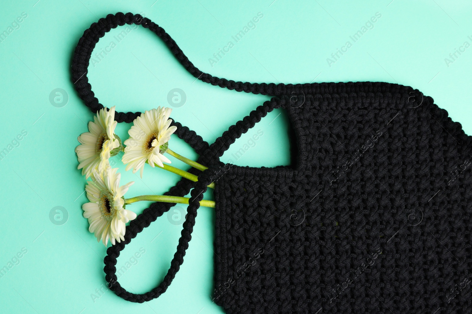 Photo of Macrame shopping bag with beautiful flowers on turquoise background, top view