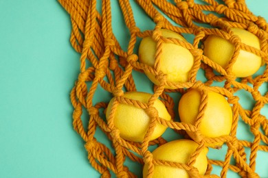 Photo of Macrame shopping bag with lemons on turquoise background, top view. Space for text