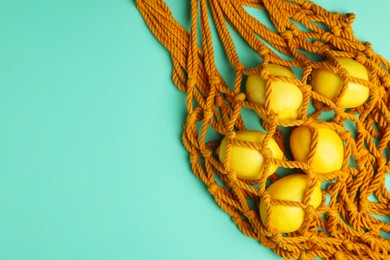 Photo of Macrame shopping bag with lemons on turquoise background, top view. Space for text