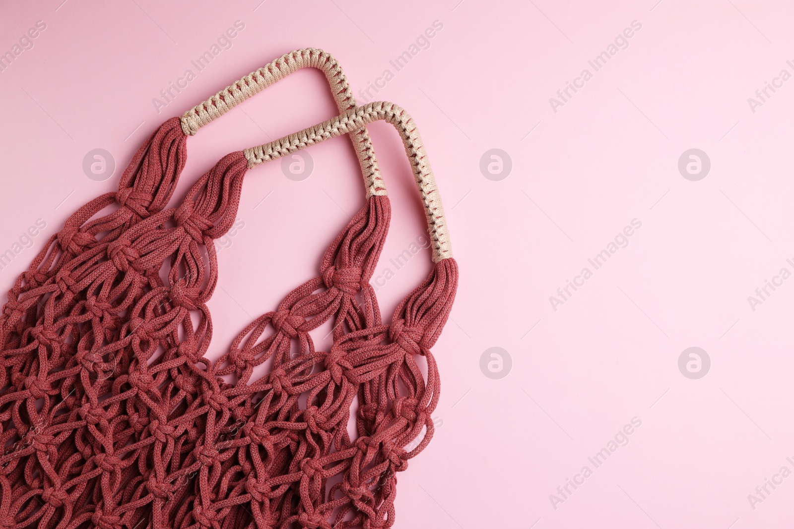 Photo of Macrame shopping bag on pink background, top view. Space for text