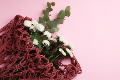 Photo of Macrame shopping bag with flowers and eucalyptus branches on pink background, top view. Space for text