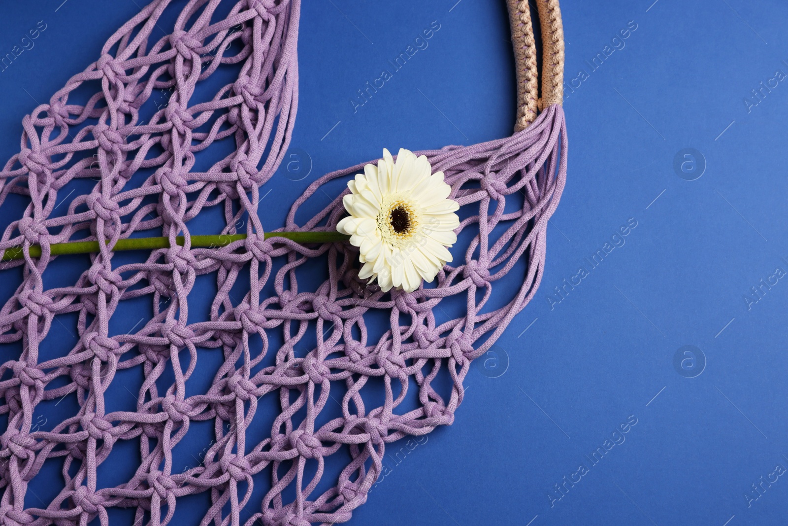 Photo of Macrame shopping bag with flower on blue background, top view. Space for text