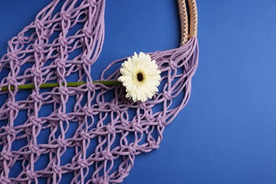 Photo of Macrame shopping bag with flower on blue background, top view. Space for text