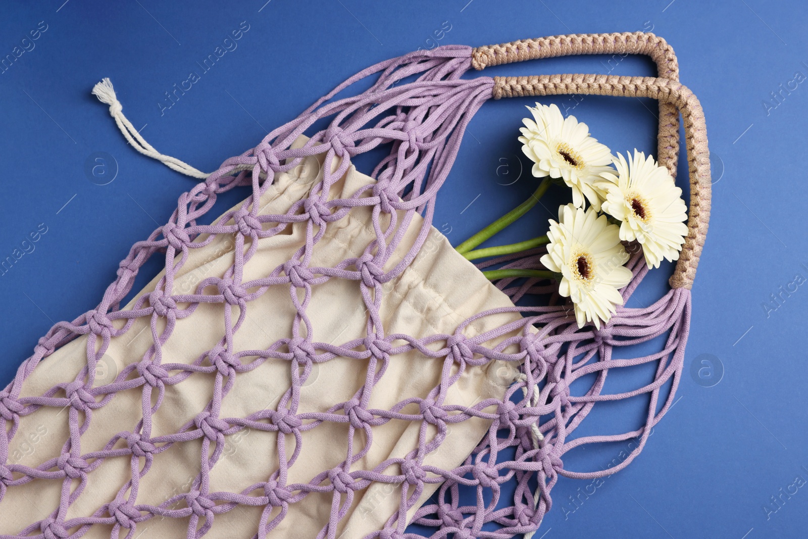 Photo of Macrame shopping bag with flowers on blue background, top view