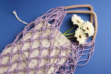 Photo of Macrame shopping bag with flowers on blue background, top view