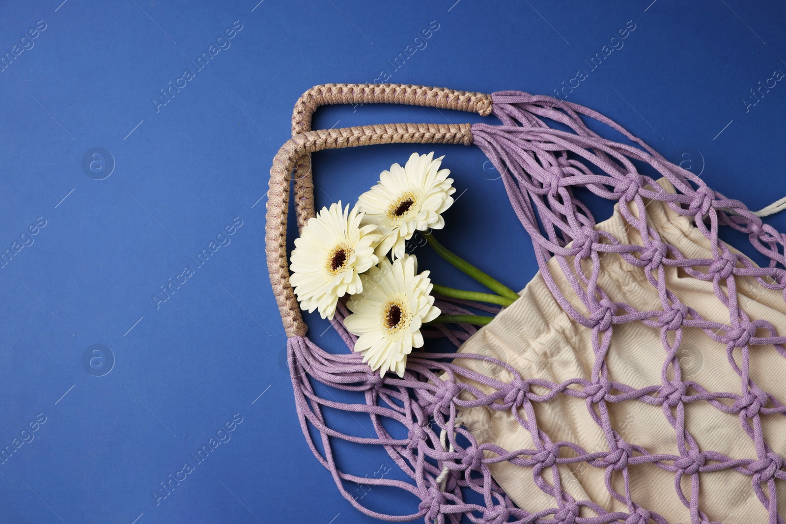 Photo of Macrame shopping bag with flowers on blue background, top view. Space for text