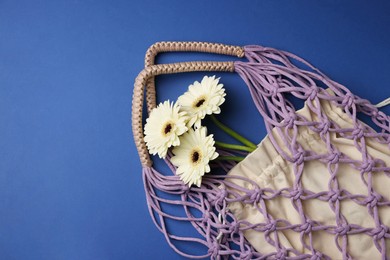 Photo of Macrame shopping bag with flowers on blue background, top view. Space for text