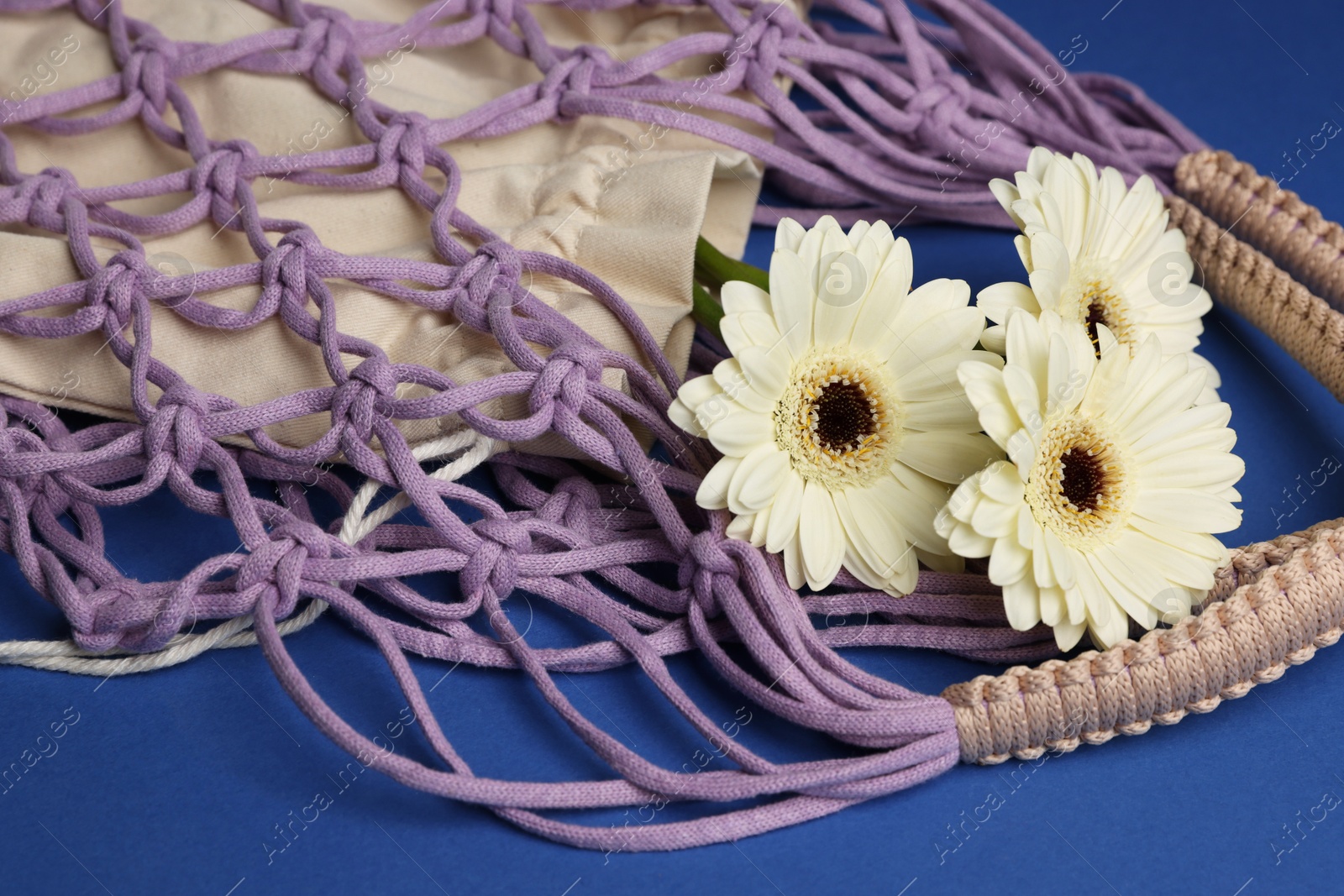 Photo of Macrame shopping bag with flowers on blue background, closeup