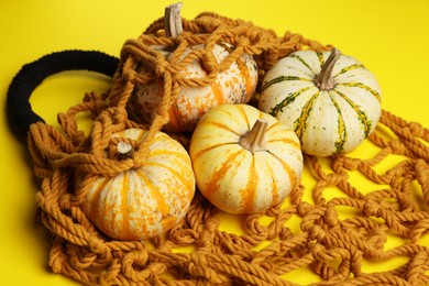 Photo of Macrame shopping bag and pumpkins on yellow background, closeup