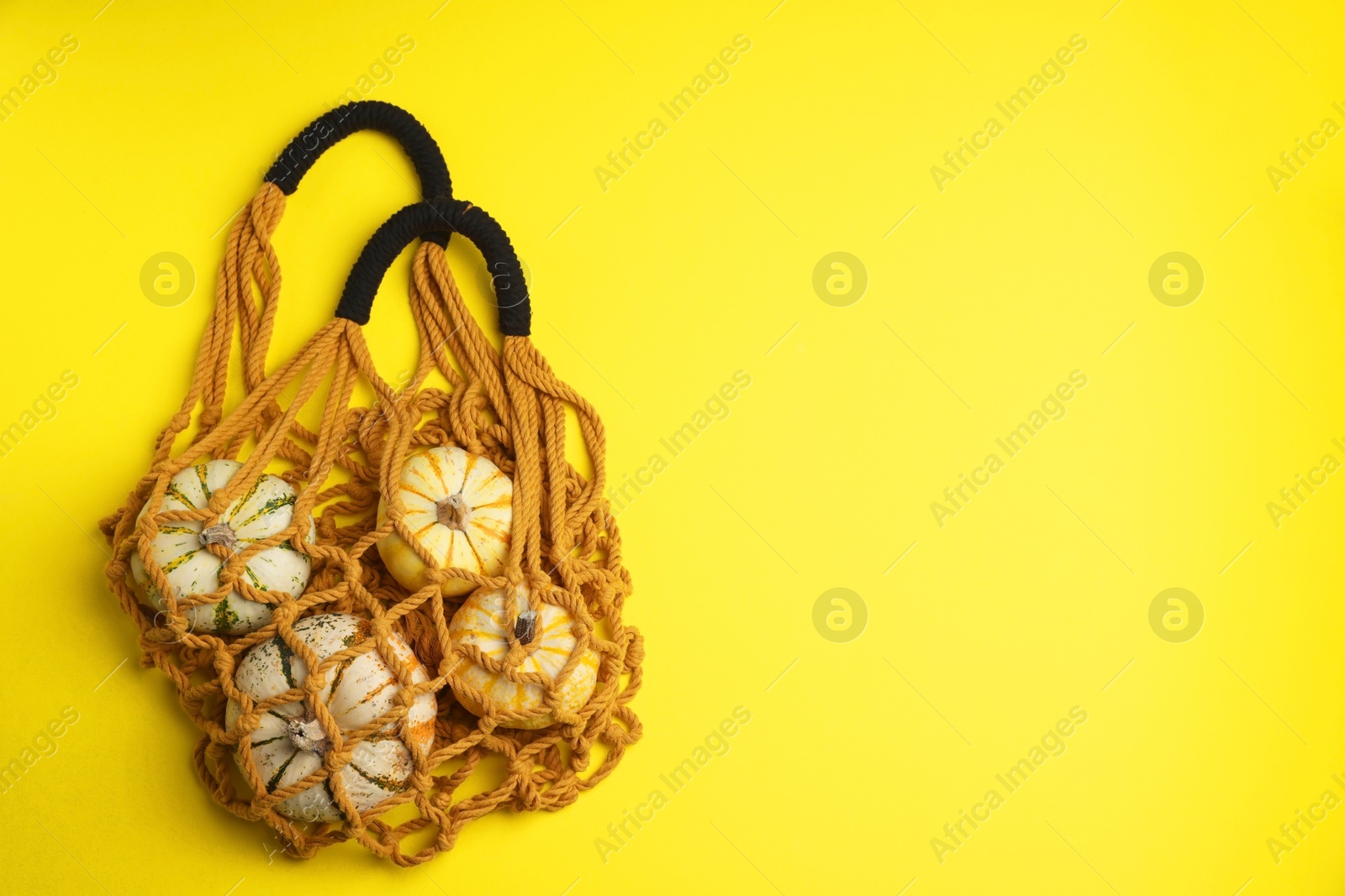 Photo of Macrame shopping bag with pumpkins on yellow background, top view. Space for text