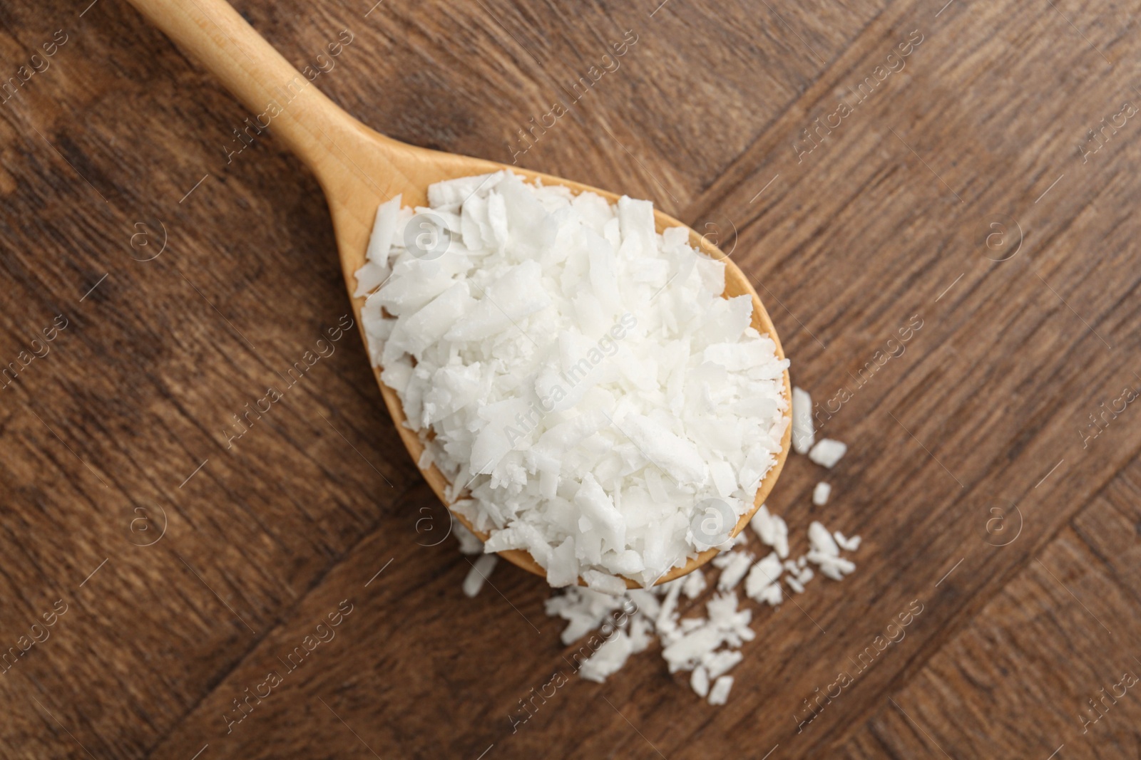 Photo of Spoon with white soy wax flakes on wooden table, top view