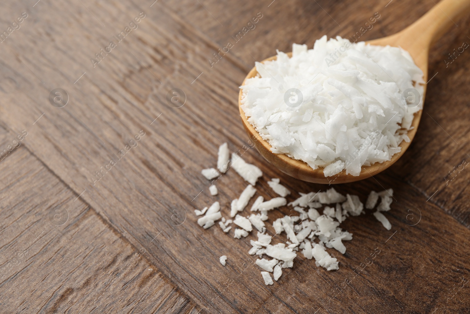 Photo of Spoon with white soy wax flakes on wooden table, closeup. Space for text