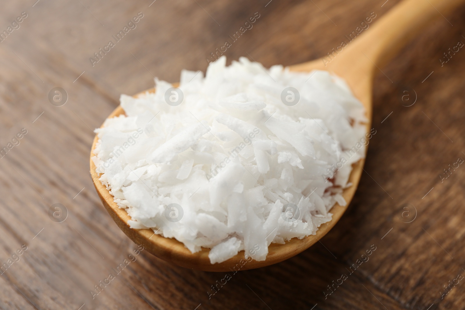 Photo of Spoon with white soy wax flakes on wooden table, closeup